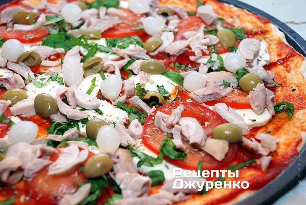 Разложить на пиццу маринованный лук и оливки.