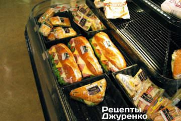 Огромный свежий батон с колбасой, помидорами, луком, маринованными огурцами, зеленым салатом, соусом.