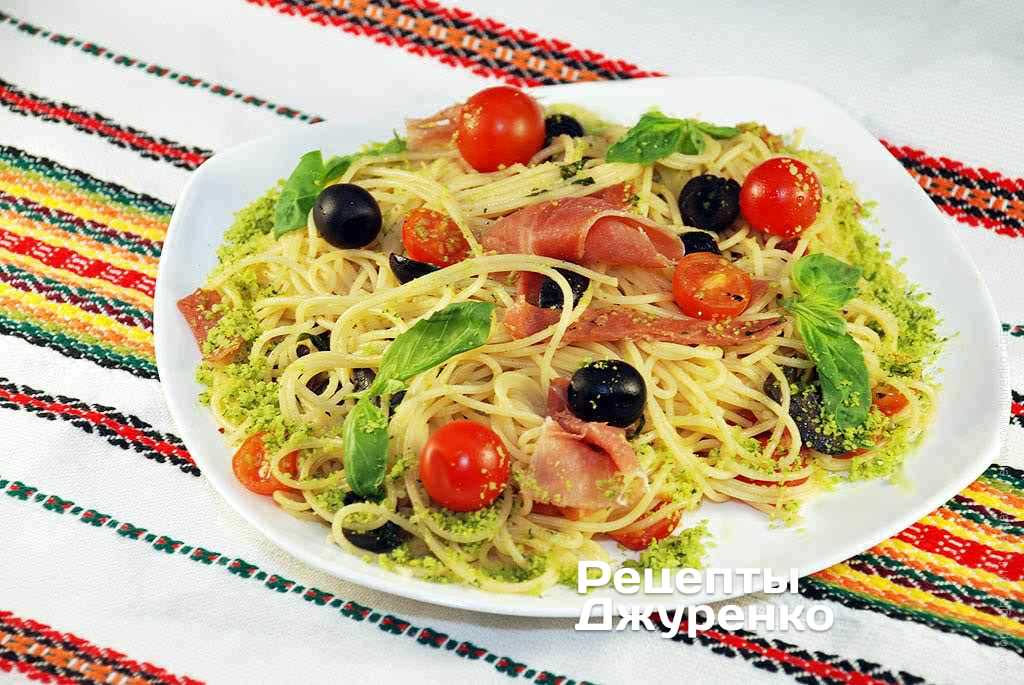 Разложит спагетти с ветчиной, помидорами и оливками на тарелки.