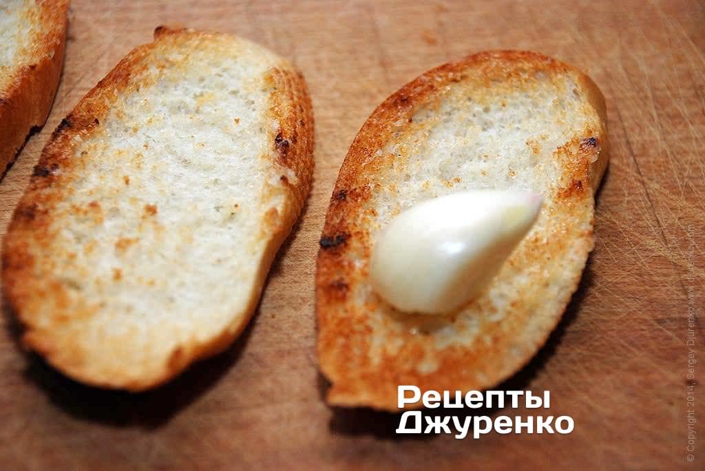 Очистить зубчик чеснока и натереть им поджаренный хлеб с одной стороны. Затем смазать натертую сторону небольшим количеством свежего оливкового масла.